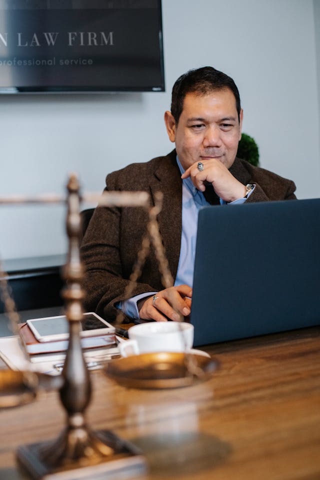 Happy Asian lawyer looking at laptop on table with tablet